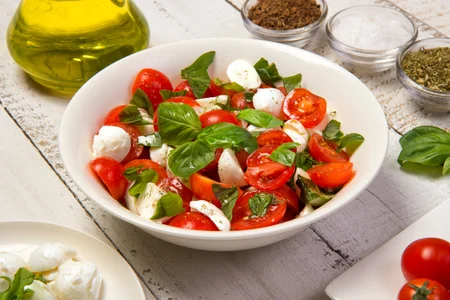 Caprese salad in a bowl on an white wooden table.