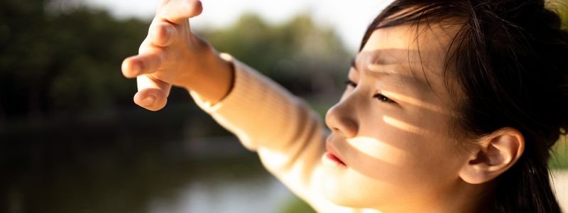 Young woman shielding her face from the sun with her hand, illustrating the importance of sun protection and daily suncare routines.