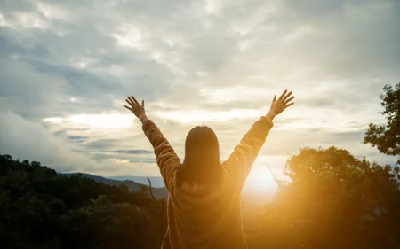 Happy woman on the sunset in nature in winter with arm raised and open hand