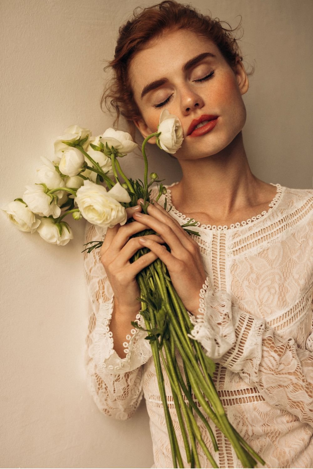 a model with her eyes closed in a wedding dress holding a bouquet of ranunculus - wedding beauty timeline
